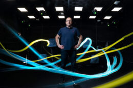 Michael Yartsev stands in a darkened room with his hands on his hips. Yellow and teal lights swirl around him.