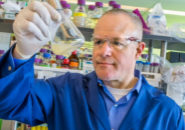 head and shoulders photo of Keasling in lab examining a flask of fluid. photo by JBEI