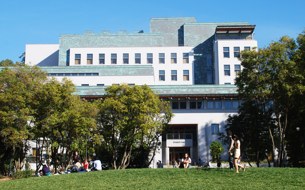 Photo of the front of Stanley Hall, a multistorey grey and green building, with students on the lawn in front