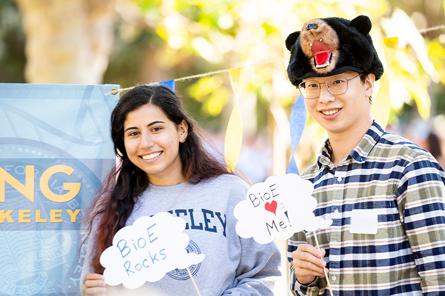 two students at the 2022 fall welcome picnic, one with an "I love BioE" sign, one with a "BioE loves me" sign